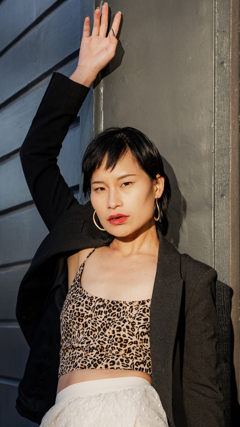 Portrait of a confident young woman standing against black background . She is posing to camera. The...