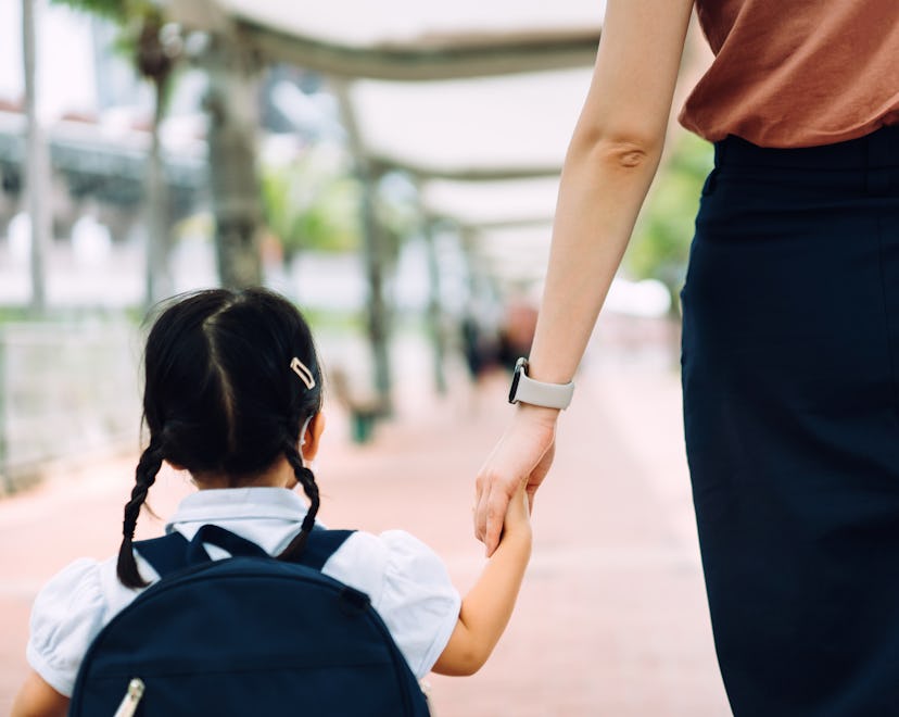 Rear view of young Asian mother taking her little daughter to school, they are holding hands and wal...