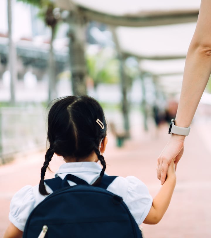 Rear view of young Asian mother taking her little daughter to school, they are holding hands and wal...