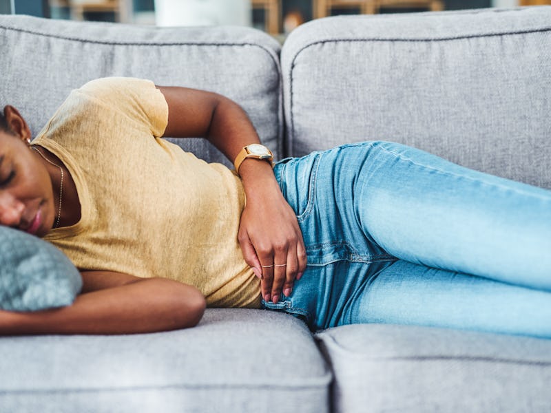 Shot of a young woman experiencing stomach pain while lying on the sofa at home