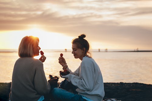 A mom and daughter eat strawberries on the beach. The July 2022 New Moon Will Affect These Zodiac Si...