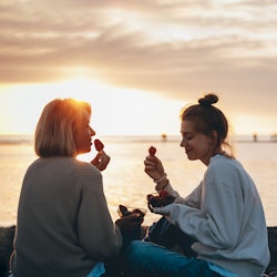 A mom and daughter eat strawberries on the beach. The July 2022 New Moon Will Affect These Zodiac Si...