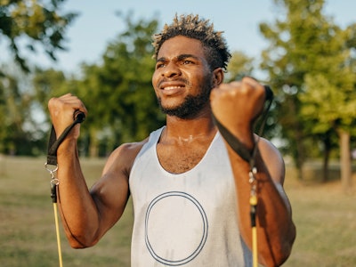 A young African American male athlete is stretching his muscles using training equipment.