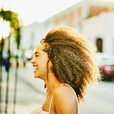 A girl with curly hair wearing a white dress smiling while the sun reflects on her hair