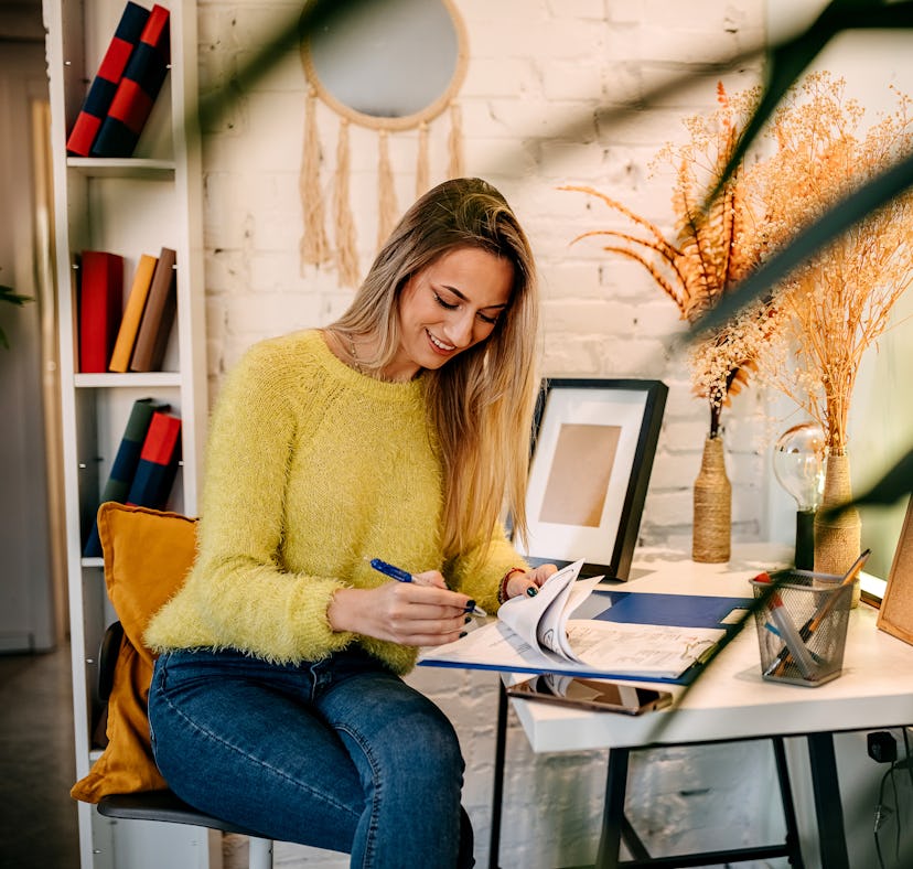 Young Caucasian woman sitting at her desk at home, looking at stock market charts on her laptop comp...