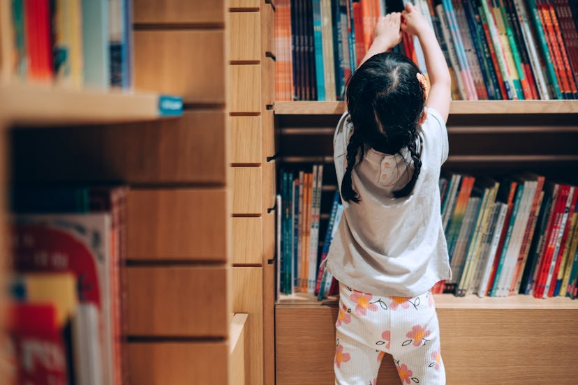 Little girl choosing books from the bookshelf at a school library in an article about how much monte...