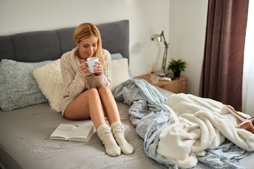 Young woman enjoying a book at home in bed while drinking coffee. Here’s your July 26 zodiac sign da...