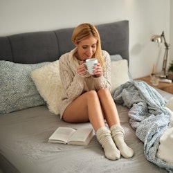 Young woman enjoying a book at home in bed while drinking coffee. Here’s your July 26 zodiac sign da...