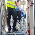 Ground service men helping wheelchair passenger to enter on airplane board, they using an elevator.