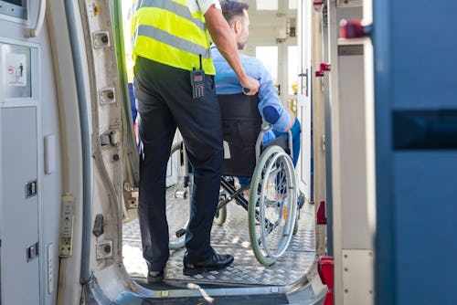 Ground service men helping wheelchair passenger to enter on airplane board, they using an elevator.