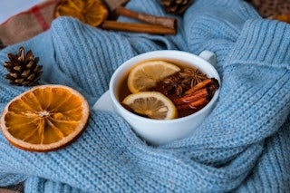 Blue sweater and cup of hot tea with lemon cinnamon sticks and anise star. Dry slices of citrus oran...