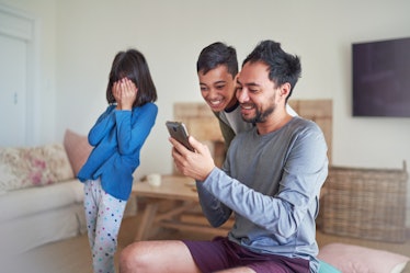 Smiling father and kids using smart phone together in living room