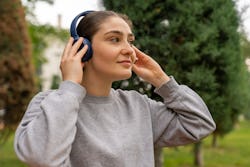 Young woman listening music from headphones in park. Here's your july 27 zodiac sign daily horoscope...