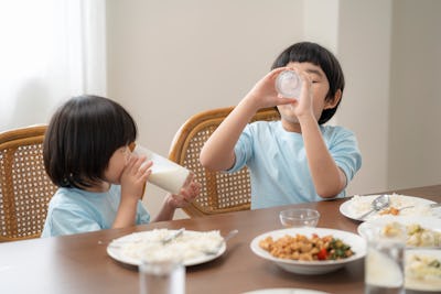 Asian children is eating milk at the dining room table, reflecting on the good relationship within t...
