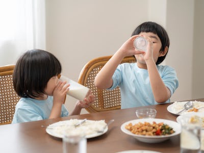 Asian children is eating milk at the dining room table, reflecting on the good relationship within t...