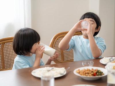 Asian children is eating milk at the dining room table, reflecting on the good relationship within t...