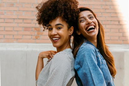 two young women back to back laugh as they discuss leo compatibility 
