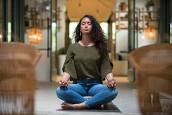 A young woman practices the lotus pose inside a yoga studio alone. Here’s your July 28 zodiac sign d...