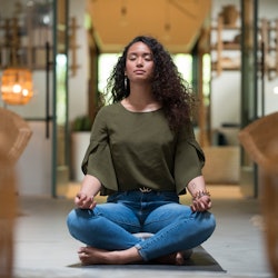 A young woman practices the lotus pose inside a yoga studio alone. Here’s your July 28 zodiac sign d...