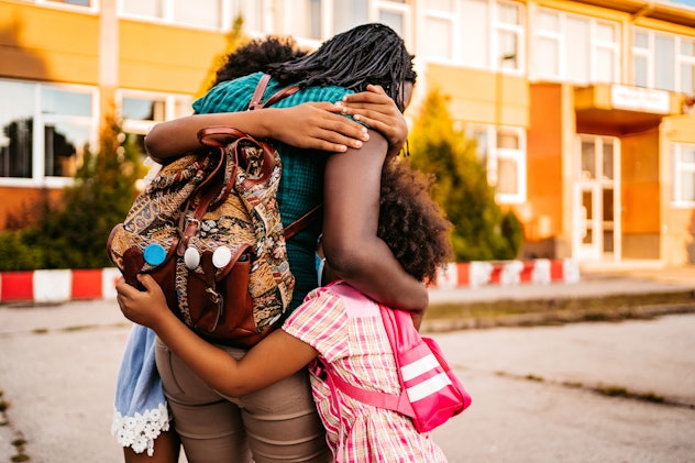 Happy daughters embracing their mother after classes in front of school. Back to school instagram ca...