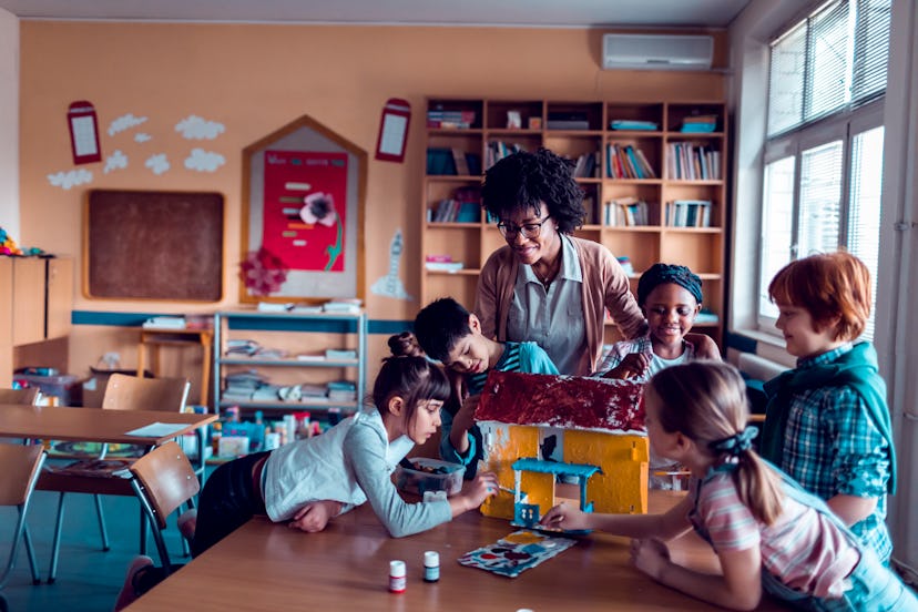 Close up of a group of elementary school kids painting a house with their teacher during arts class ...