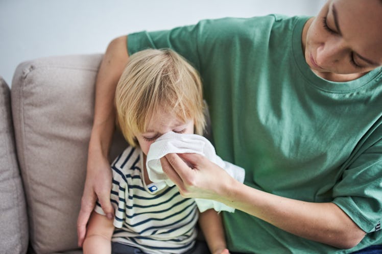A young mother using a white handkerchief to blow her child’s nose