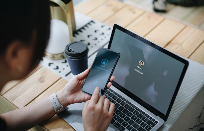 Young Asian businesswoman working on desk, logging in to her laptop and holding smartphone on hand w...