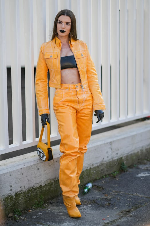 Julia Fox wears a black shiny leather shoulder-off / cropped top, an orange shiny varnished leather …