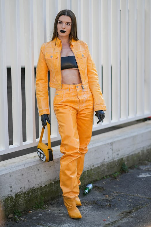 Julia Fox wears a black shiny leather shoulder-off / cropped top, an orange shiny varnished leather ...