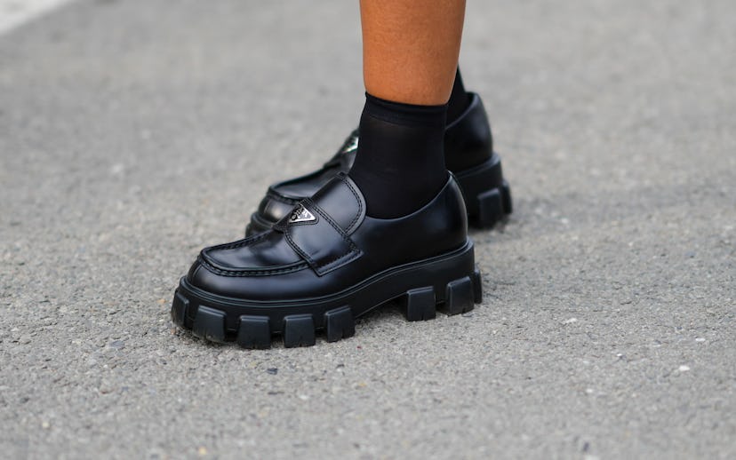 MILAN, ITALY - FEBRUARY 24: A guest wears black socks, black shiny leather loafers from Prada, outsi...