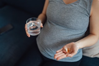 Close up of woman taking postnatal vitamin and  nutrition supplement with water. Pregnancy health ca...
