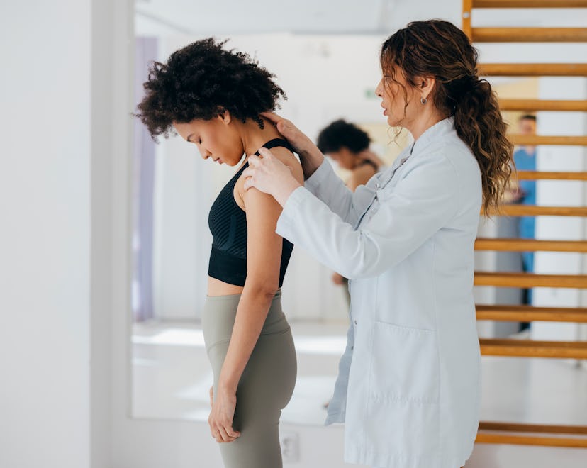 Side view of modern rehabilitation physiotherapy worker helping young female client with spine injur...