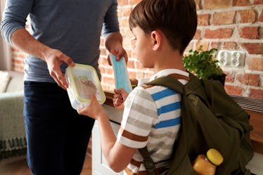 A father gives his kid a lunch box while he prepares for school as part of his morning routine