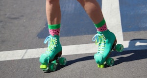 A pair of teal-colored roller skates on a city street. With green, pink and black “watermelon-look” ...