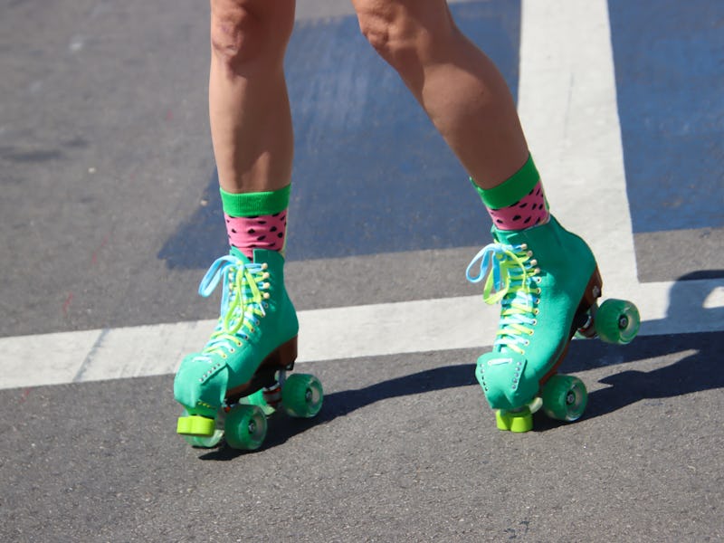 A pair of teal-colored roller skates on a city street. With green, pink and black “watermelon-look” ...