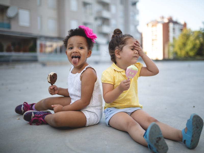 Cute and lovely mixed race siblings enjoying their time together in a city public park, eating ice c...