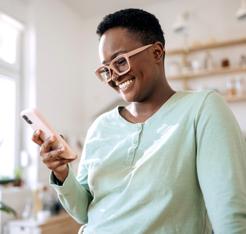 A woman on her phone in her kitchen is looking at weird but genius Amazon kitchen must-haves going v...
