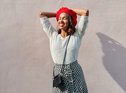 young woman wearing red bedet smiles as she thinks about her upcoming july 11, 2022 weekly horoscope