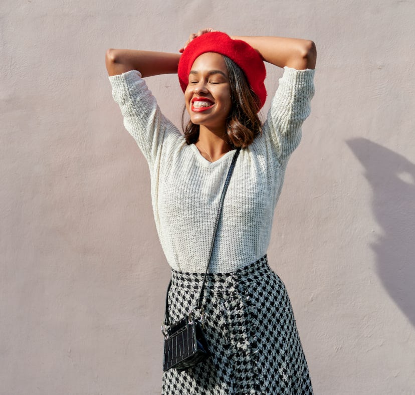 young woman wearing red bedet smiles as she thinks about her upcoming july 11, 2022 weekly horoscope