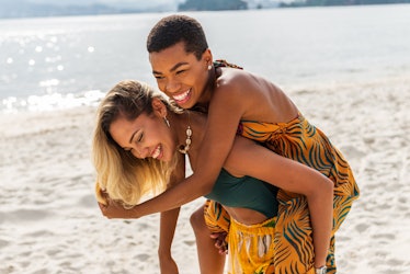 two young women enjoy giving each other piggyback rides on the beach as they chat about their july 1...
