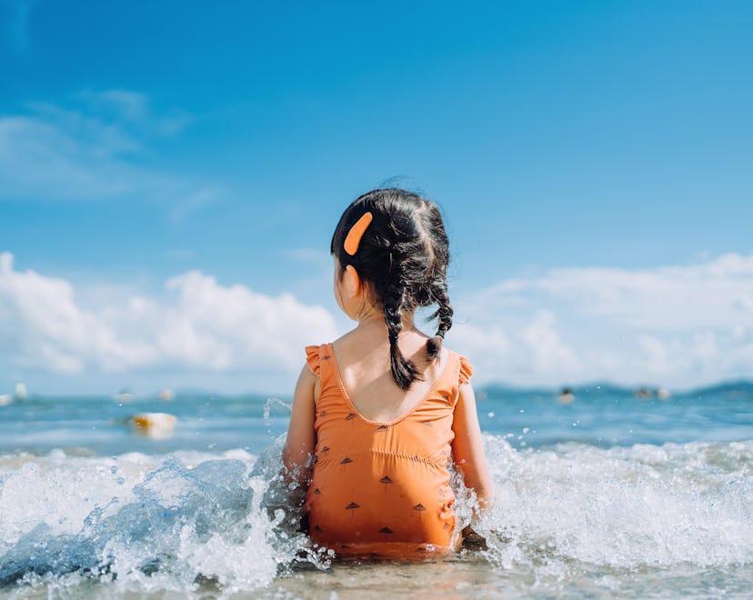 toddler in cute swimsuit sitting in the water at the beach