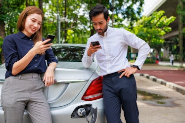 Two business person playing smartphone waiting their car for electric charge. Sustainable and renewa...