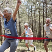 Happy senior woman celebrating the first place while crossing the finish line of a marathon in natur...