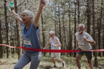 Happy senior woman celebrating the first place while crossing the finish line of a marathon in natur...