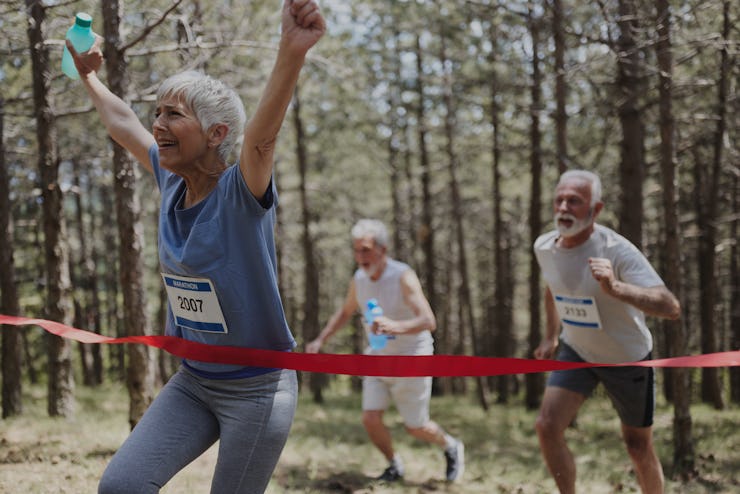 Happy senior woman celebrating the first place while crossing the finish line of a marathon in natur...