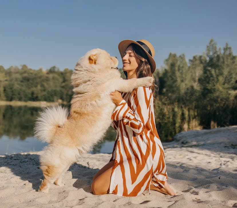 Young woman wearing blouse and hat playing with the dog by the lake during Mercury retrograde fall 2...