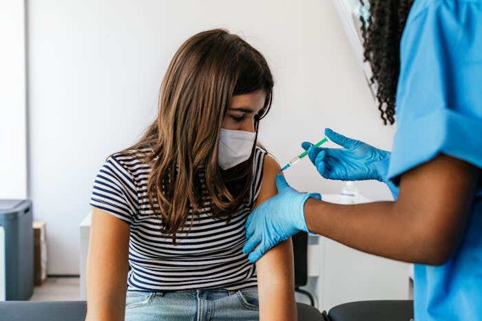 Front view of a preteen girl sitting in examination table receiving a vaccine at a medical clinic.