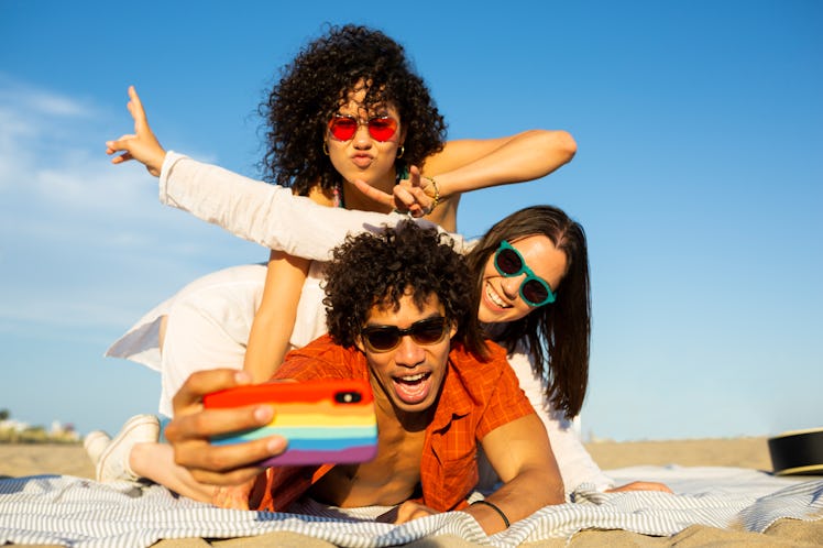 Group of multi ethnic friends, two women and a man, taking a selfie with an smartphone and hanging o...