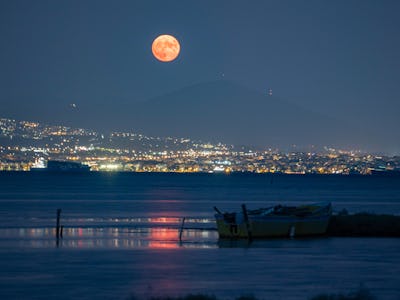 The moon with the city lights and local fishing boats. The August Sturgeon full moon rises behind th...