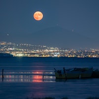 The moon with the city lights and local fishing boats. The August Sturgeon full moon rises behind th...